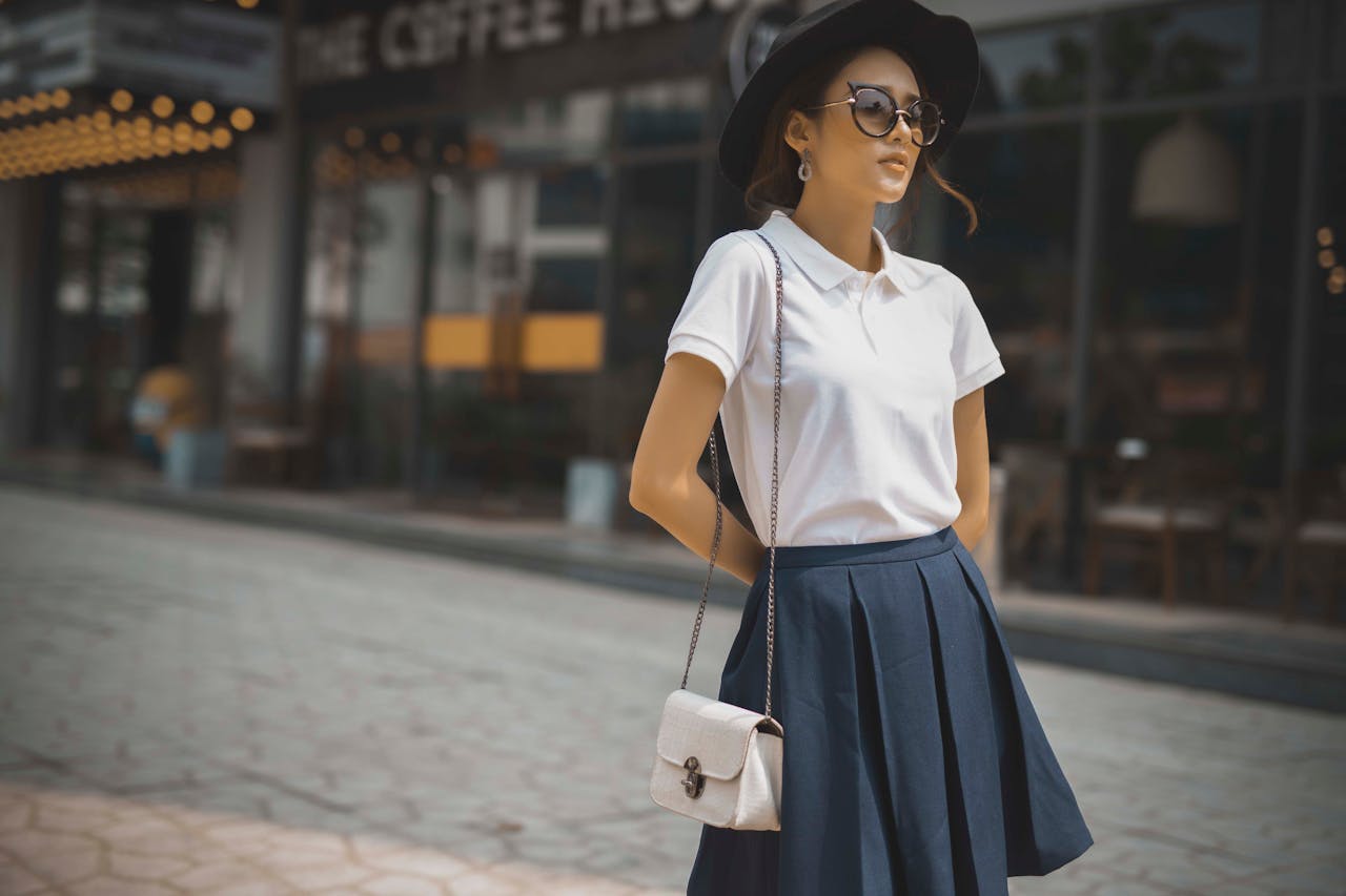 creative Stylish woman in white polo and skirt, posing with confidence on a city street.
